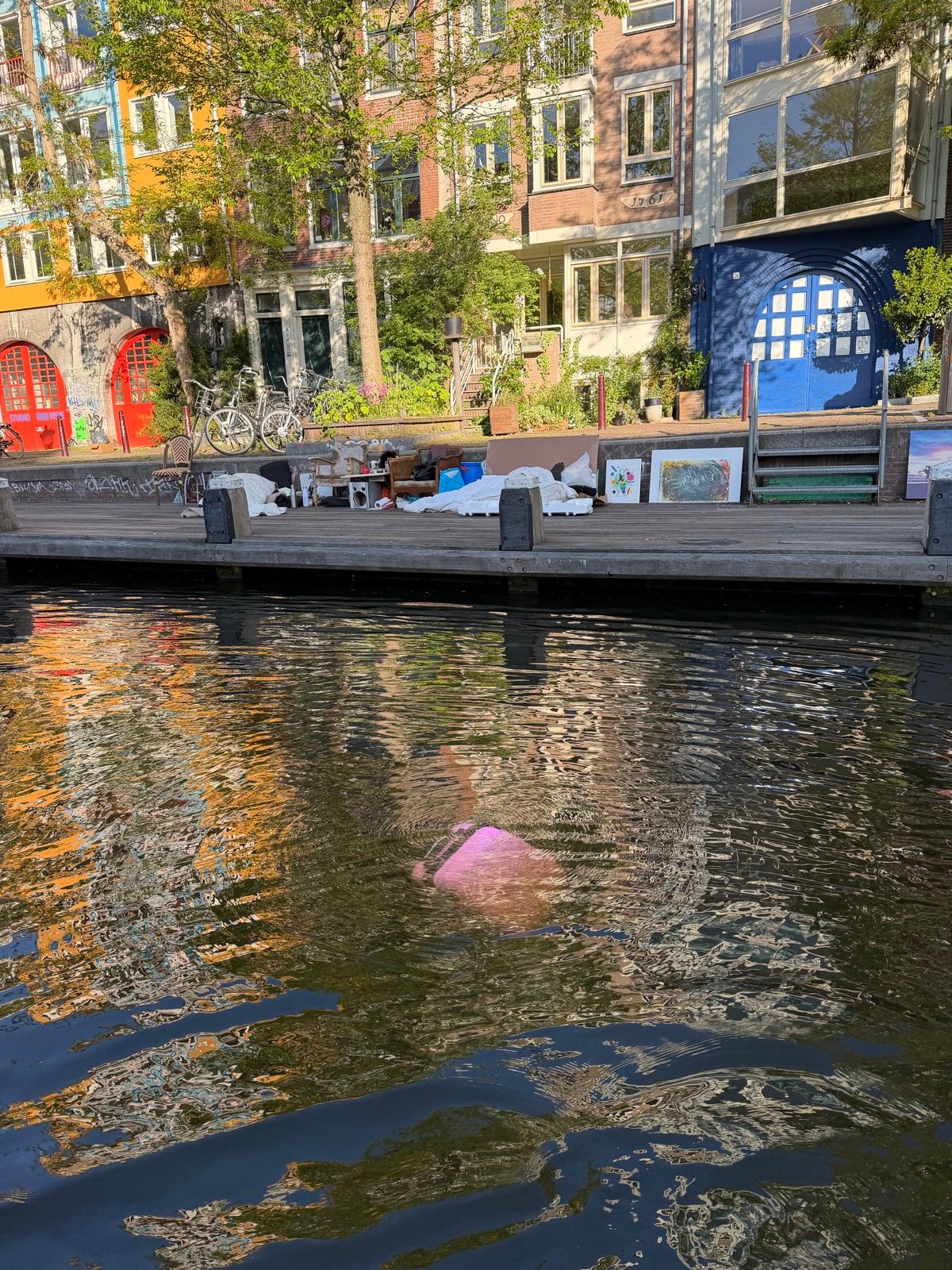 A vibrant canal scene features colorful buildings reflecting in the water, with a wooden dock in the foreground