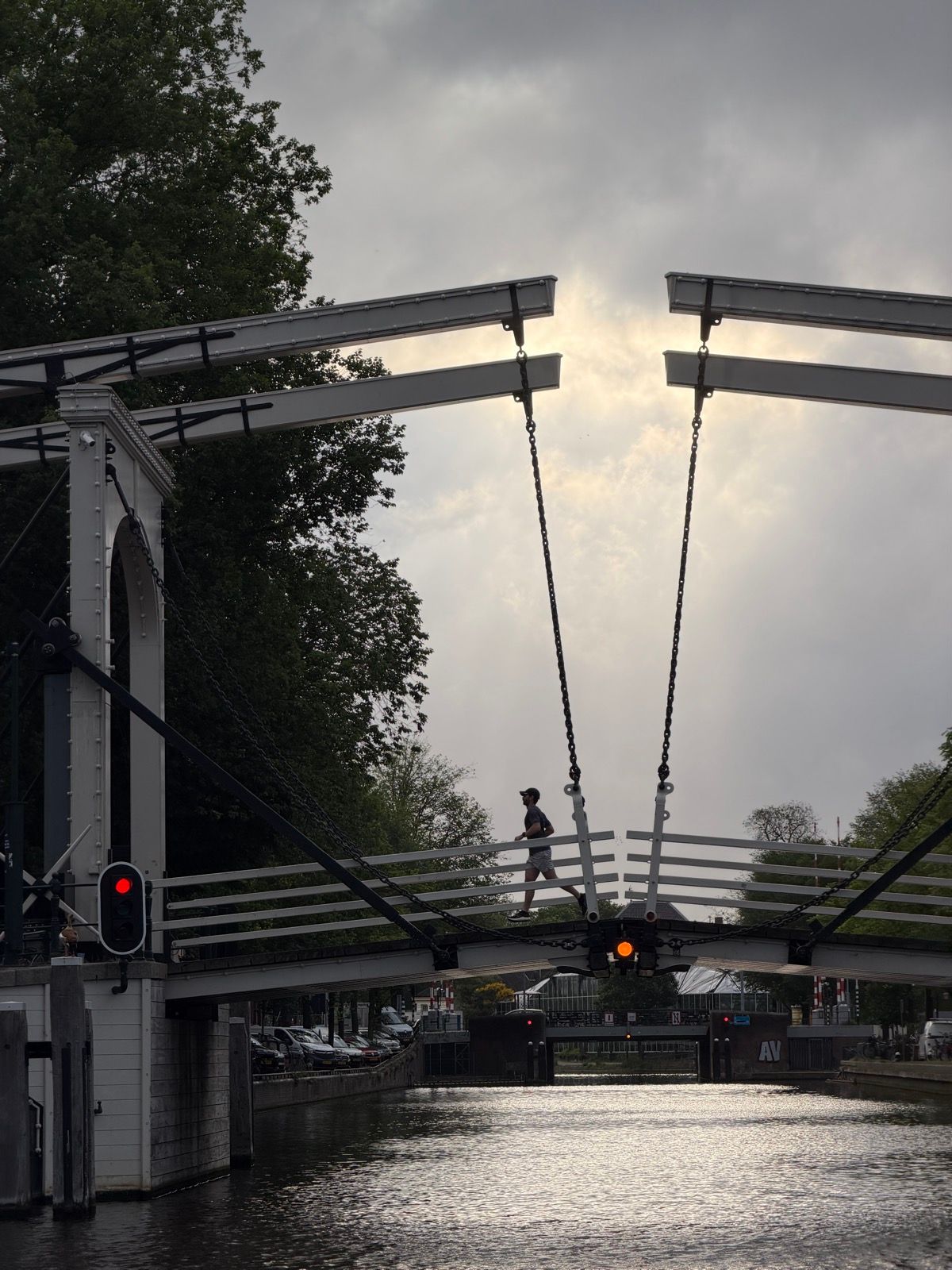 A lone figure jogs across a white drawbridge spanning a canal, silhouetted against a bright, cloudy sky during golden hour