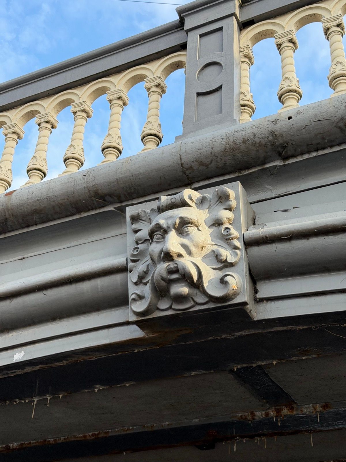 A detailed close-up shot captures an ornate architectural carving, a mascaron, on the side of a grey bridge structure