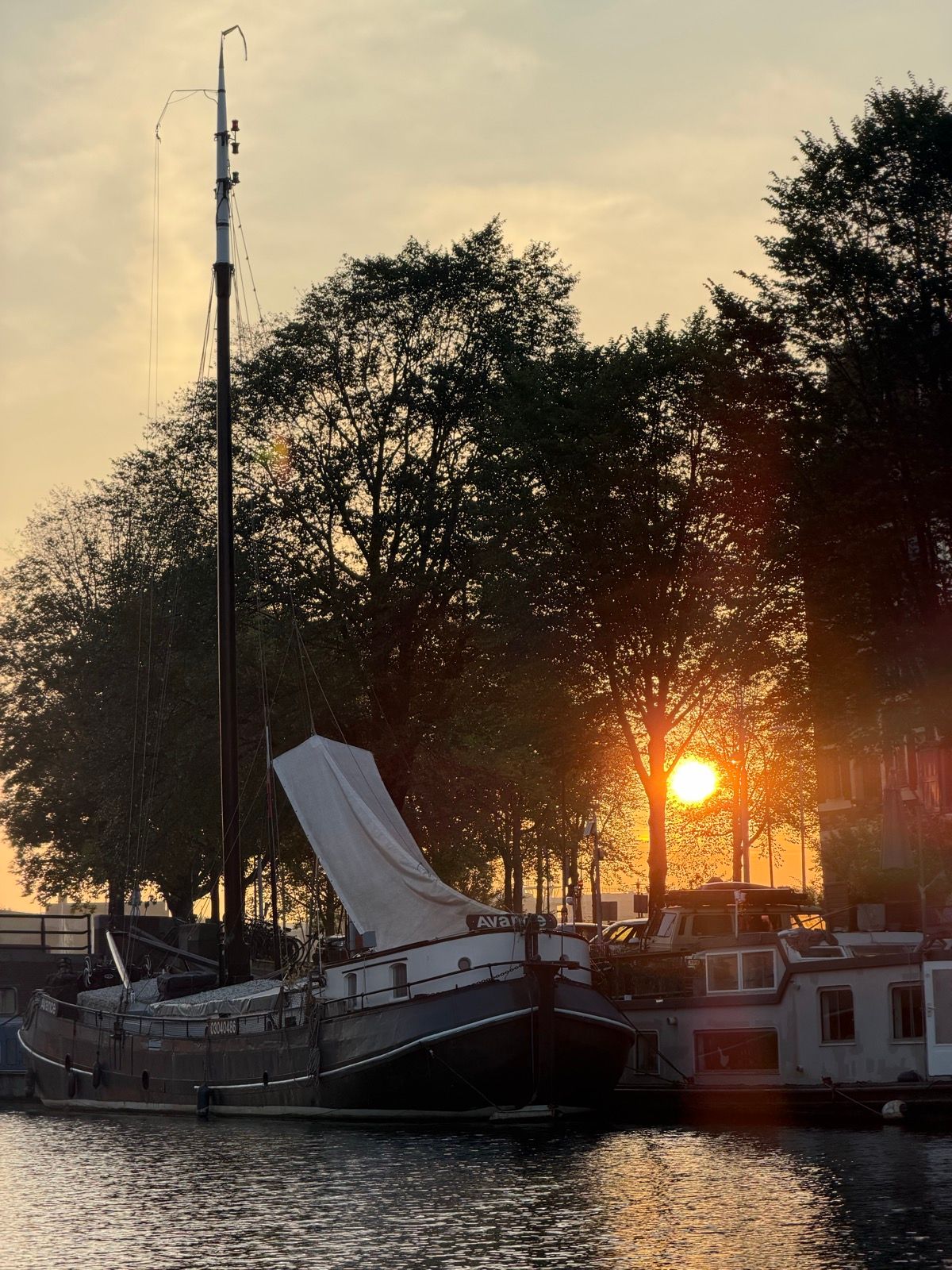 A beautiful sunset casts a warm golden glow over a tranquil canal, where several boats are peacefully docked